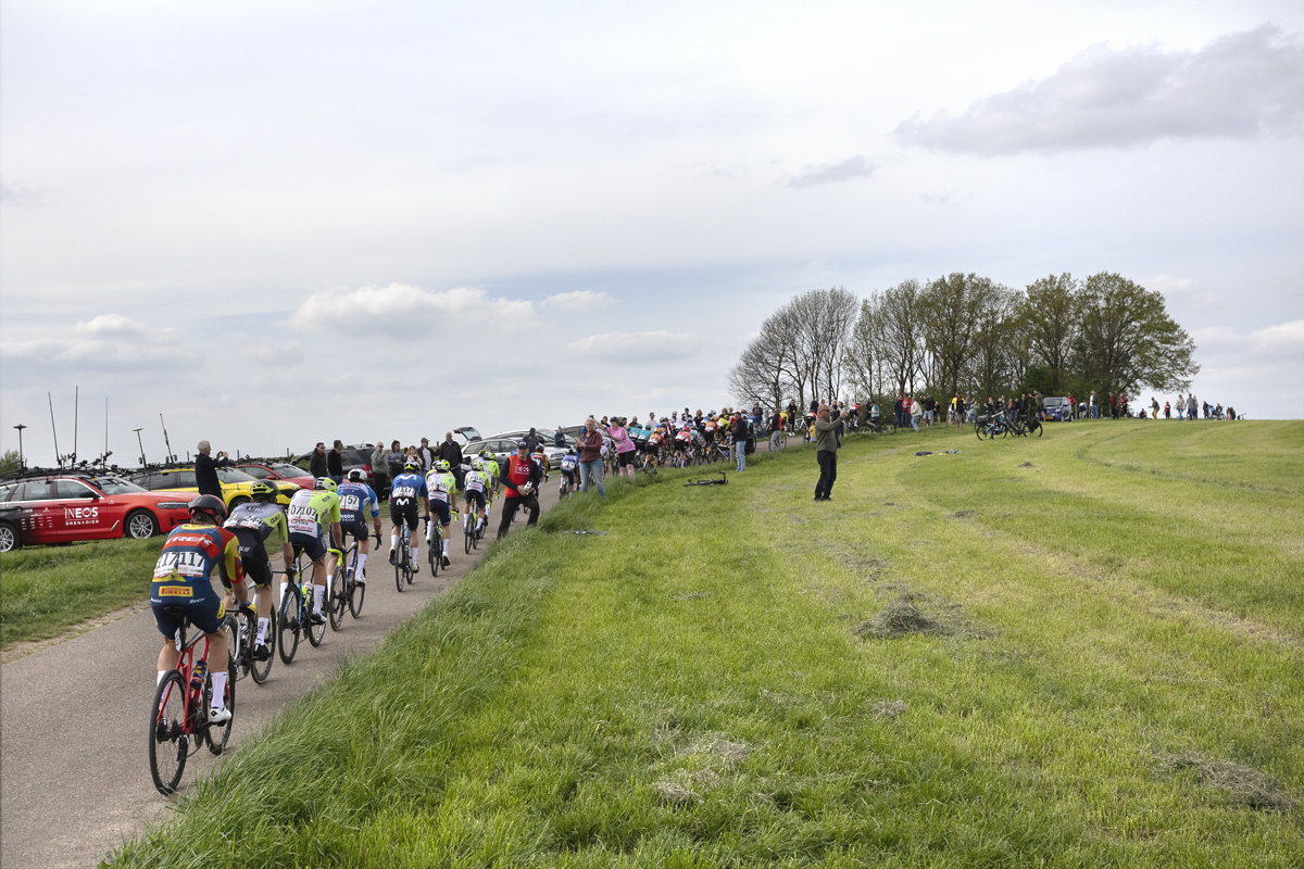 Amstel Gold Race 2024 - Riders pass team cars lined up on the crest of a climb on Schaapsdries