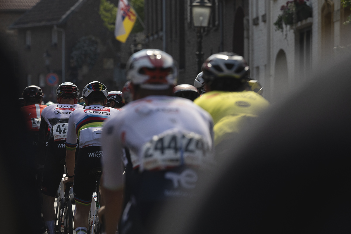 Amstel Gold Race 2025 - A rear view of the peloton as it makes its way through Elsloo, a Limburg flag flying in the distance