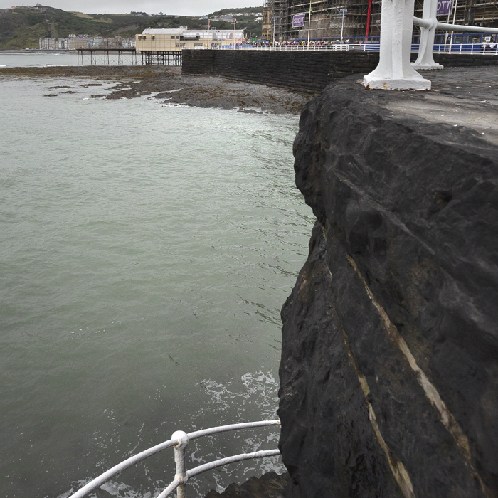 British National Road Championships 2025 - Road Race - Men - Aberystwyth - the men’s race seen from a distance with the sea in the foreground and steps leading down to the water