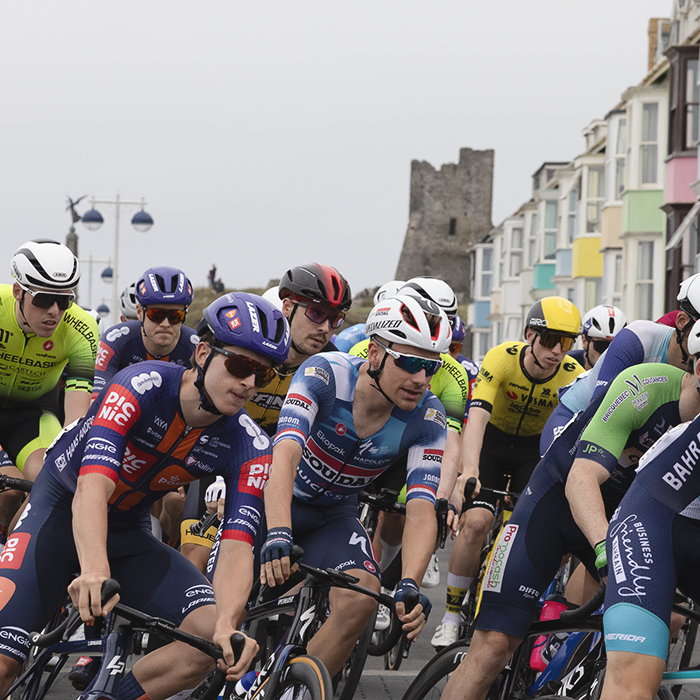 British National Road Championships 2025 - Road Race - Men - Aberystwyth - riders round a corner past brightly coloured house, castle in the background