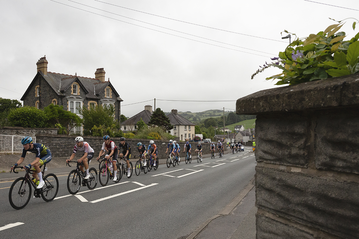 British National Road Championships 2025 - Road Race - Men - a group of riders race through the streets of Llanfarian
