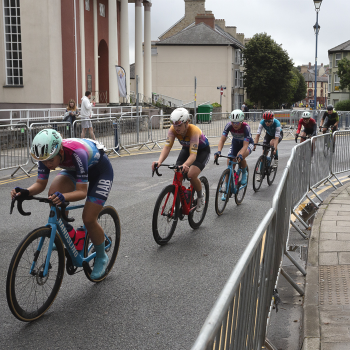 British National Road Championships 2025 - Road Race - Women - Aberystwyth - riders race through the streets past a building with columns