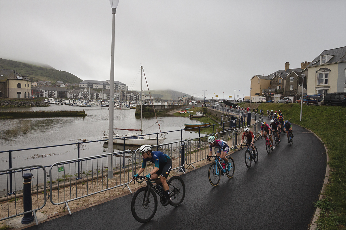 British National Road Championships 2025 - Road Race - Women - Aberystwyth - riders pass the old harbour with boats bobbing on the water
