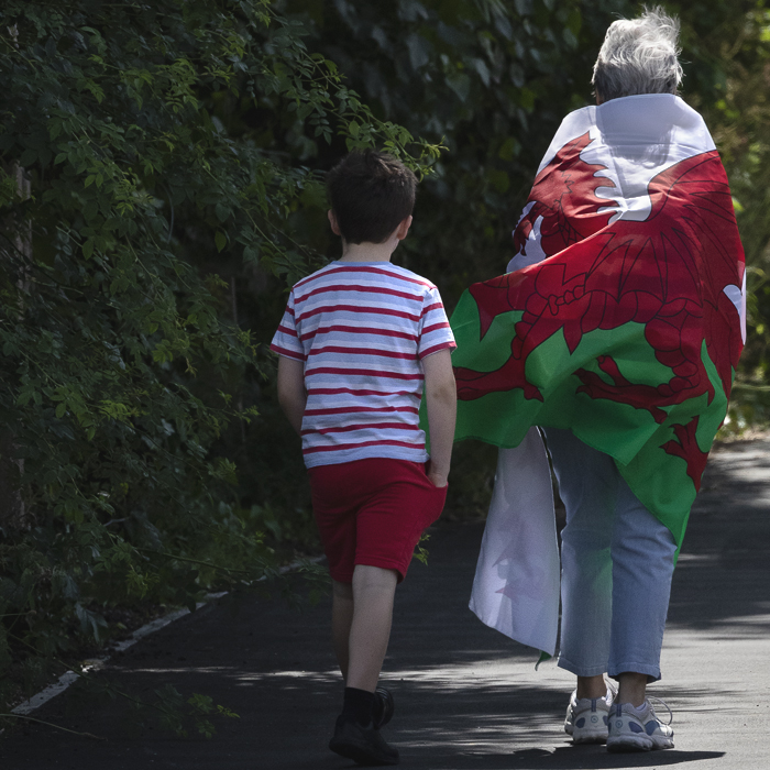 British National Road Championships 2025 - Time Trial - U23 Women - an older women wearing a Welsh flag as a cloak walks along the path accompanied by a young boy