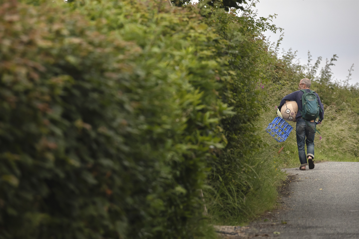 British National Road Championships 2025 - Time Trial - U23 Men - a fan walks down the road holding the Papier-mâché head he was wearing under his arm