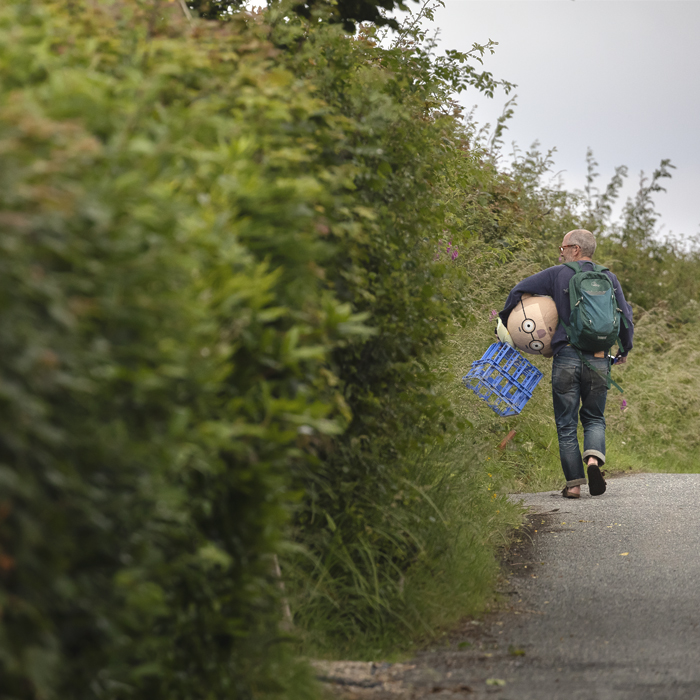 British National Road Championships 2025 - Time Trial - U23 Men - a fan walks down the road holding the Papier-mâché head he was wearing under his arm