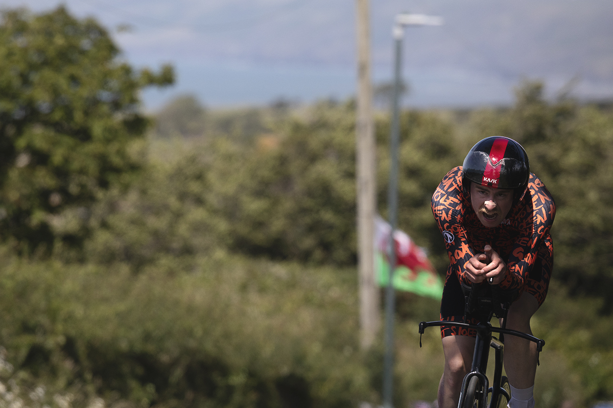 British National Road Championships 2025 - Time Trial - Elite Men - Ben Goodwin of Stolen Goat Race Team pushes up a hill while a Welsh flag flys in the background