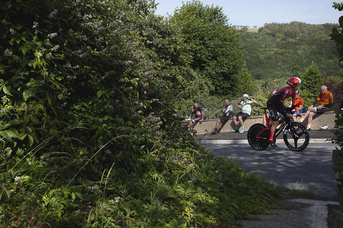 British National Road Championships 2025 - Time Trial - Elite Men - Sam Watson of Ineos Grenadiers is watched by a group of amateur cyclists from a wall at the roadside