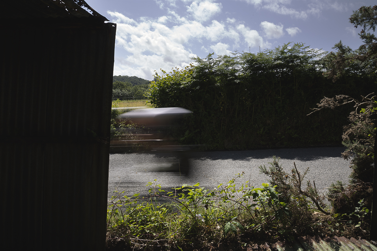 British National Road Championships 2025 - Time Trial - Elite Women - a rider seen through an old shed speeding past