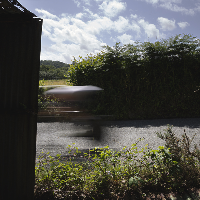 British National Road Championships 2025 - Time Trial - Elite Women - a rider seen through an old shed speeding past