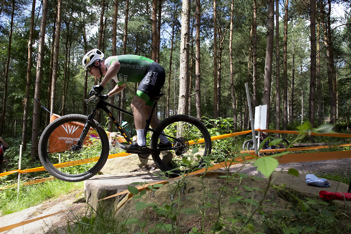 Birmingham 2022 - XXII Commonwealth Games - Mountain Bike - Men - Christopher Mcglinchey of Northern Ireland takes a jump with the Commonwealth Games logo framed in his front wheel