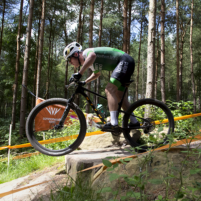 Birmingham 2022 - XXII Commonwealth Games - Mountain Bike - Men - Christopher Mcglinchey of Northern Ireland takes a jump with the Commonwealth Games logo framed in his front wheel