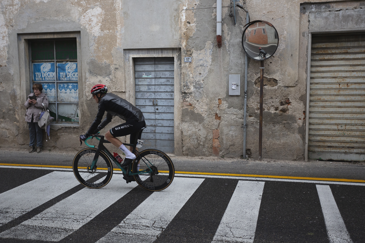 Coppa Bernocchi 2024 - Louis Barré rides over a zebra crossing as a woman looks at her phone while leaning against a window displaying election posters