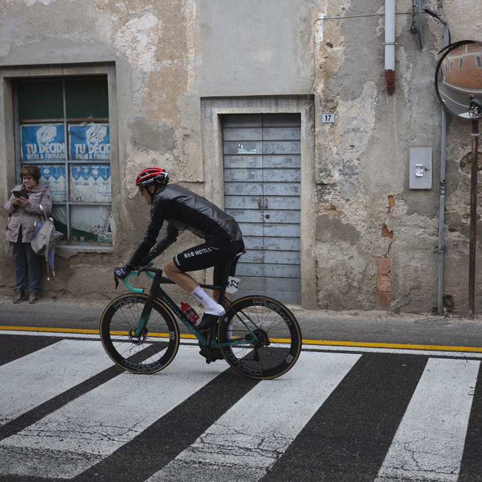 Coppa Bernocchi 2024 - Louis Barré rides over a zebra crossing as a woman looks at her phone while leaning against a window displaying election posters