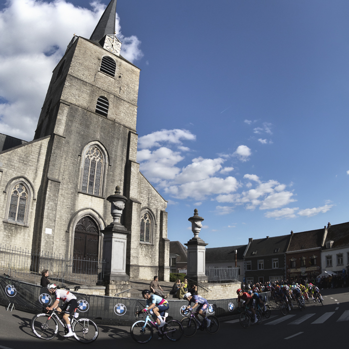 De Brabantse Pijl 2024 - A group of riders emerge from the shadows past Sint-Martinus Kerk and round a corner