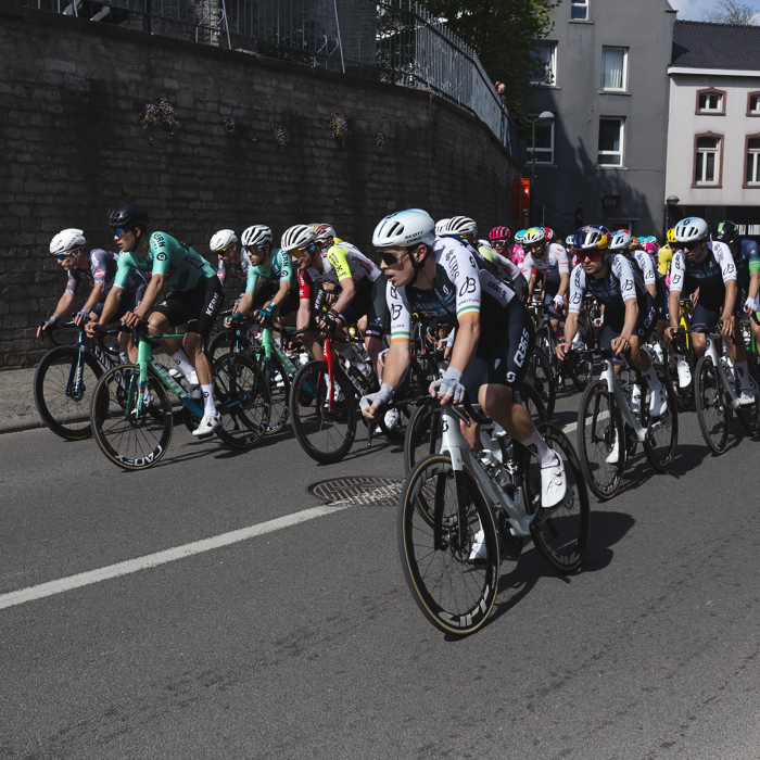 De Brabantse Pijl 2025 - The peloton passes a wall at the base of the church in Overijse