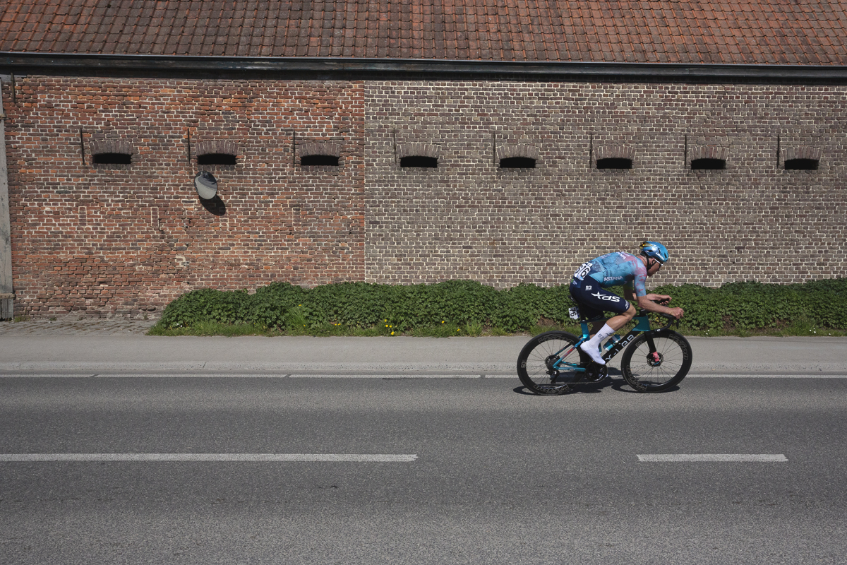 Dwars Door Vlaanderen 2025 - Mike Teunissen rides past the side of a brick built barn