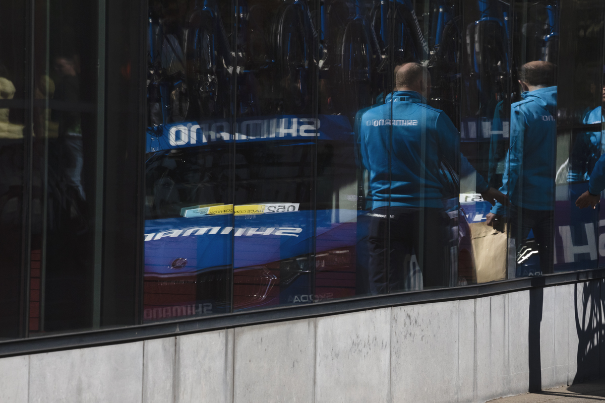Dwars Door Vlaanderen 2025 - The neutral service vehicle and mechanics are reflected in the window of a building