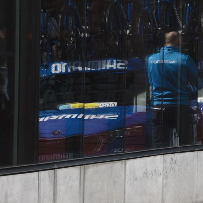Dwars Door Vlaanderen 2025 - The neutral service vehicle and mechanics are reflected in the window of a building