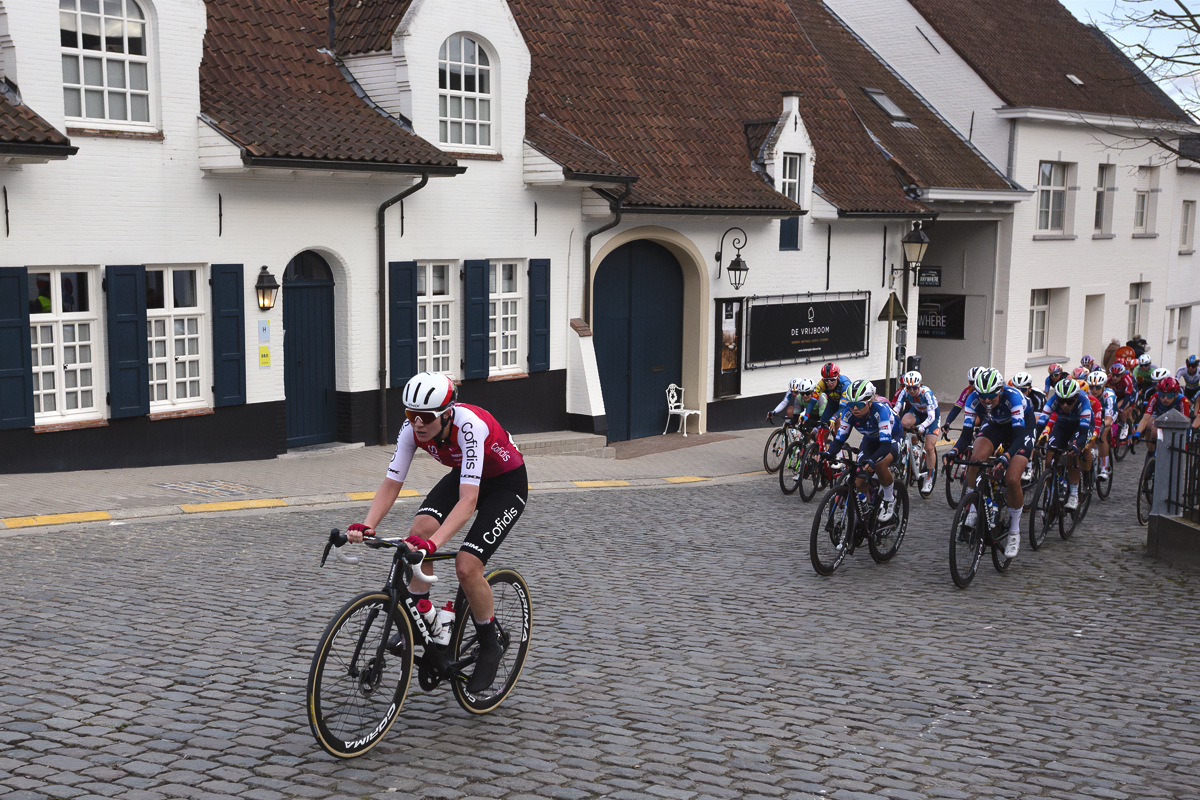 Dwars Door Vlaanderen Vrouwen 2024 - Riders climb through Nokere with a white washed traditional building behind them