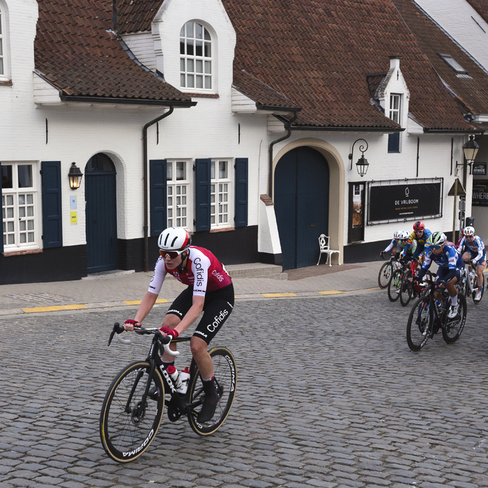 Dwars Door Vlaanderen Vrouwen 2024 - Riders climb through Nokere with a white washed traditional building behind them
