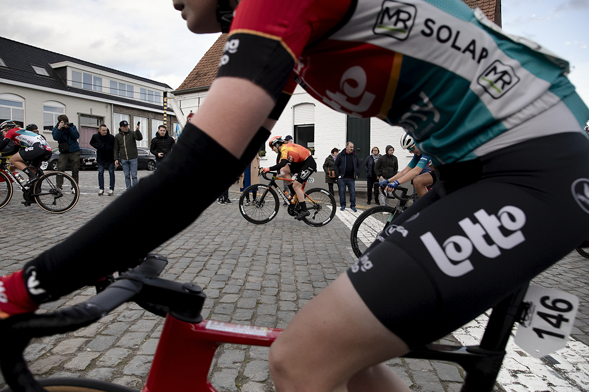 Dwars Door Vlaanderen Vrouwen 2024 - A rider is framed through the form of another as they climb Nokereberg