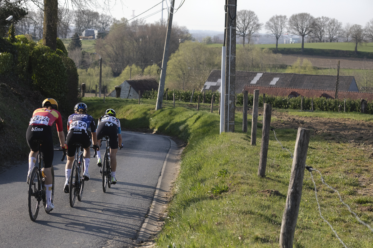 Dwars Door Vlaanderen Vrouwen 2025 - Riders from behind descending on a banked road