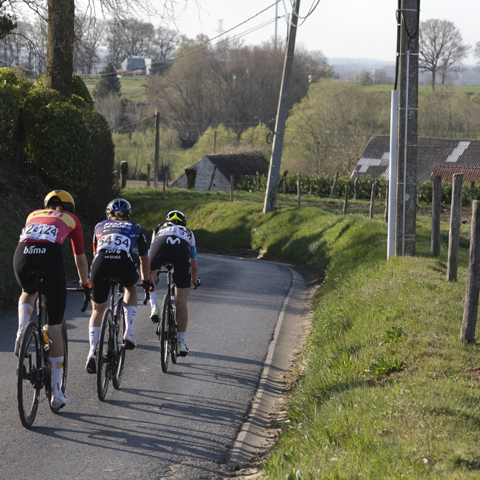 Dwars Door Vlaanderen Vrouwen 2025 - Riders from behind descending on a banked road