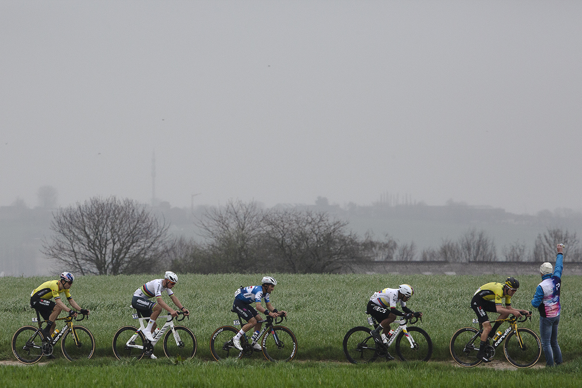 E3 Saxo Classic 2024 - A soigneur holds up a bidon for passing riders on Aaste Heerweg
