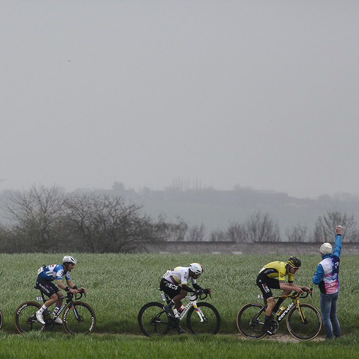 E3 Saxo Classic 2024 - A soigneur holds up a bidon for passing riders on Aaste Heerweg