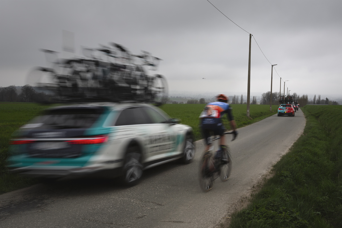 E3 Saxo Classic 2024 - A rider in the convoy of team cars speeds down Langekouter