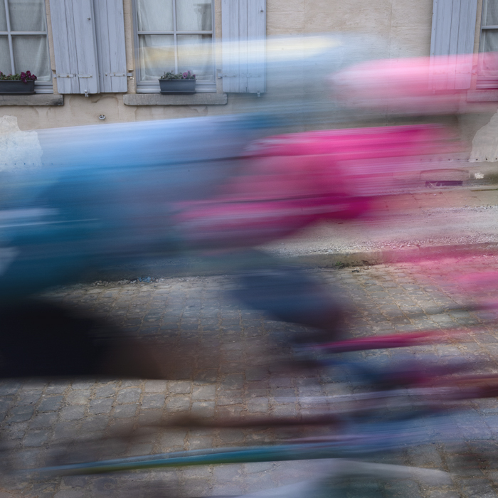 E3 Saxo Classic 2025 - Riders speed past a traditional building with blue shutters as they begin the Stationberg climb