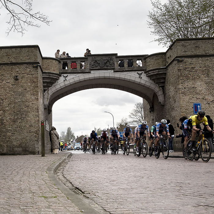 Gent Wevelgem 2024 - Riders pass through Rijselpoort while fans watch from a vantage point on top of the gateway