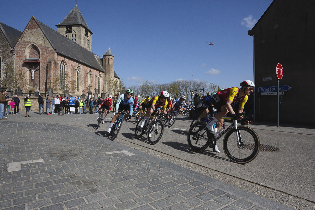 Gent Wevelgem 2025 - The peloton takes a corner with the church of Sint Vedastuskerk in the background