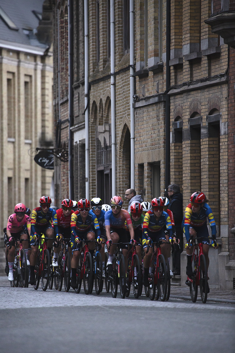 Gent Wevelgem Vrouwen 2024 - Riders on a street enclosed by tall brick buildings in Ieper / Ypres