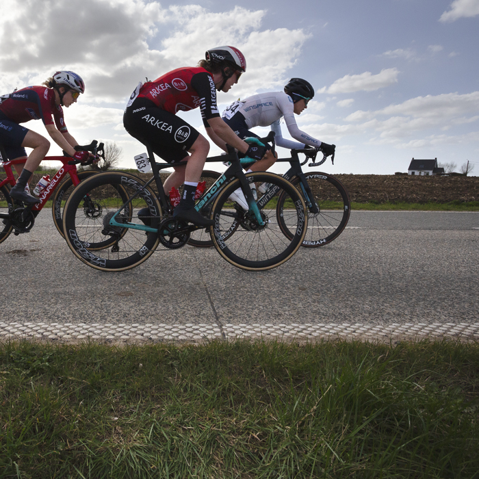 Gent Wevelgem Vrouwen 2025 - Riders in Loker with a small white cottage in the distance