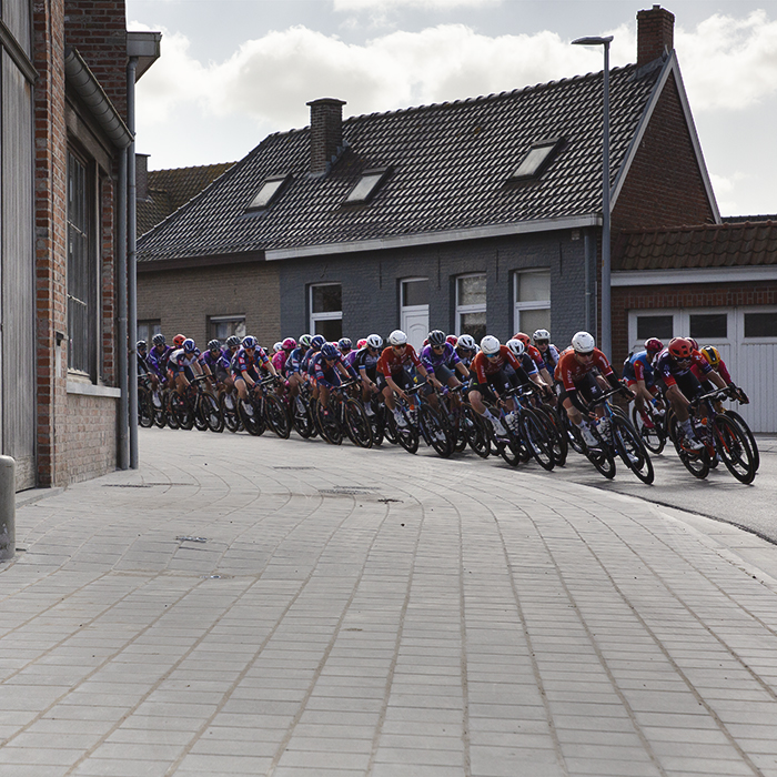 Gent Wevelgem Vrouwen 2025 - The peloton rounds a corner in Reningelst past typically Belgian buildings