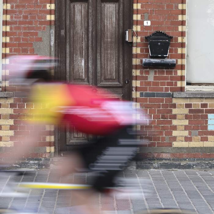 Gent Wevelgem Vrouwen 2025 - A Cofidis rider speeds past an old brick building in Reningelst