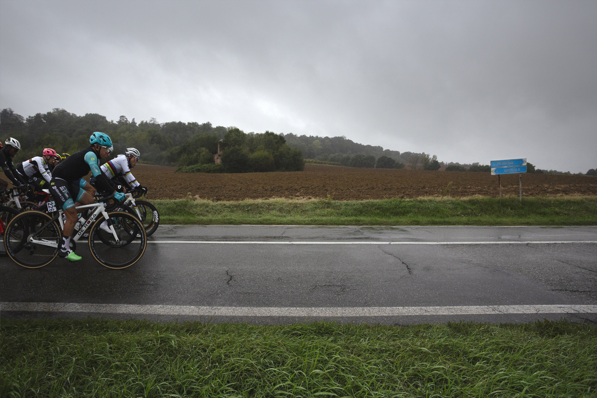 Giro dell’Emilia 2024 - The front of the peloton with World Champion Tadej Pogačar against ploughed fields and a ruined farm house in Castelvetro