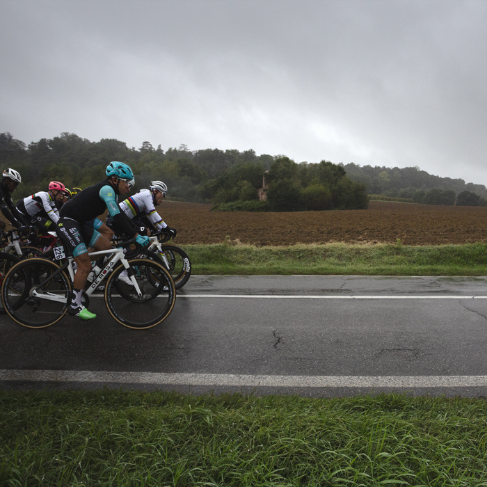 Giro dell’Emilia 2024 - The front of the peloton with World Champion Tadej Pogačar against ploughed fields and a ruined farm house in Castelvetro