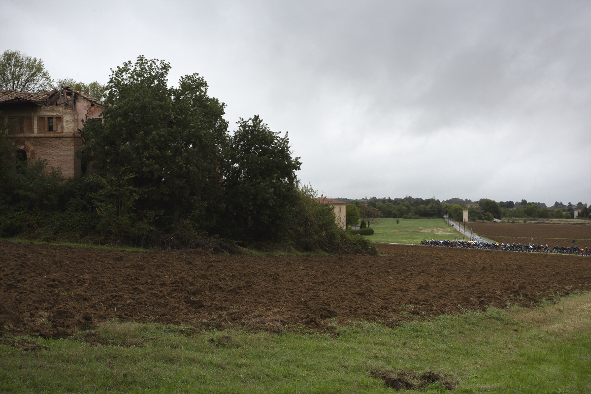 Giro dell’Emilia 2024 - The peloton in the distance with a runied farmhouse in the foreground in Castelvetro