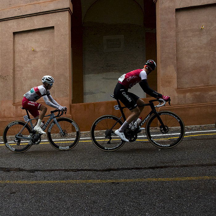 Giro dell’Emilia 2024 - A group of three riders ride past the terracotta portico on Via di San Luca