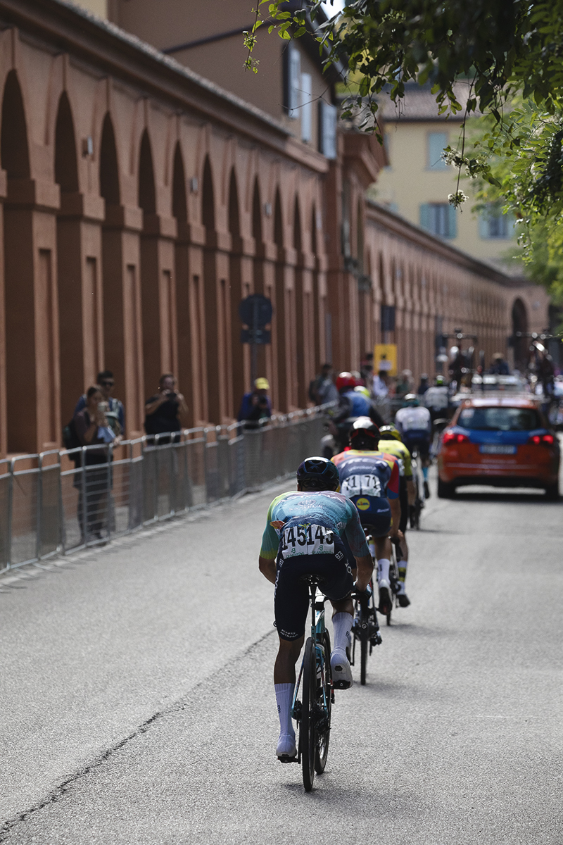 Giro dell’Emilia 2025 - Riders from behind on the climb with the Portico stretching out into the distance