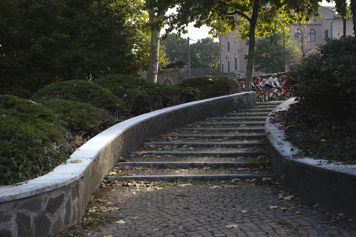 Giro dell’Emilia 2025 - The peloton viewed from the bottom of a curved set of steps in Mirandola