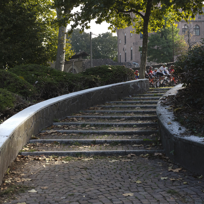Giro dell’Emilia 2025 - The peloton viewed from the bottom of a curved set of steps in Mirandola