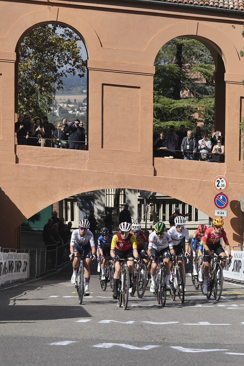 Giro dell'Emilia Internazionale Donne Elite 2025 - A lead group passes under one of the arches on the portico as fans look down from above