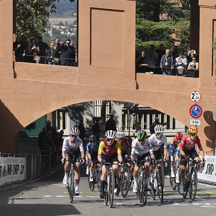 Giro dell'Emilia Internazionale Donne Elite 2025 - A lead group passes under one of the arches on the portico as fans look down from above