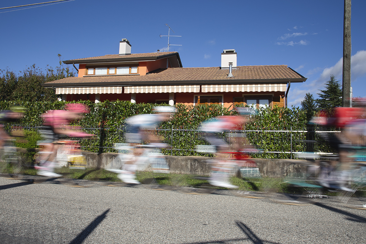 Gran Piemonte 2024 - Riders speed past an orange coloured house in Maggiora