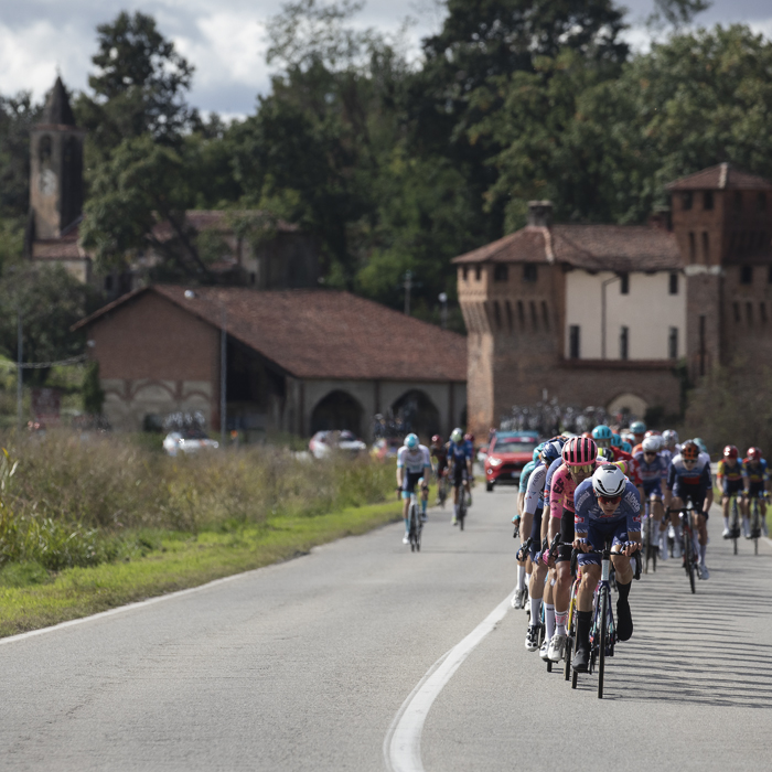 Gran Piemonte 2024 - A group of riders head down the road with the impressive Castello di Proh and a village church tower as the backdrop