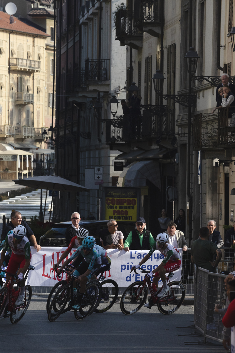 Gran Piemonte 2025 - A group of riders round a corner in Acqui Terme